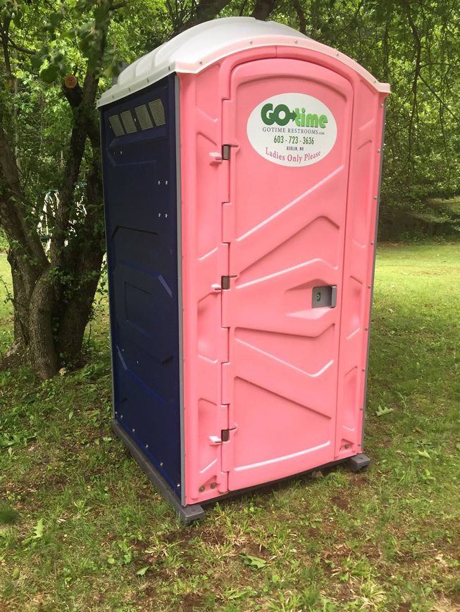 Pink and blue portable toilet in a grassy outdoor setting; 