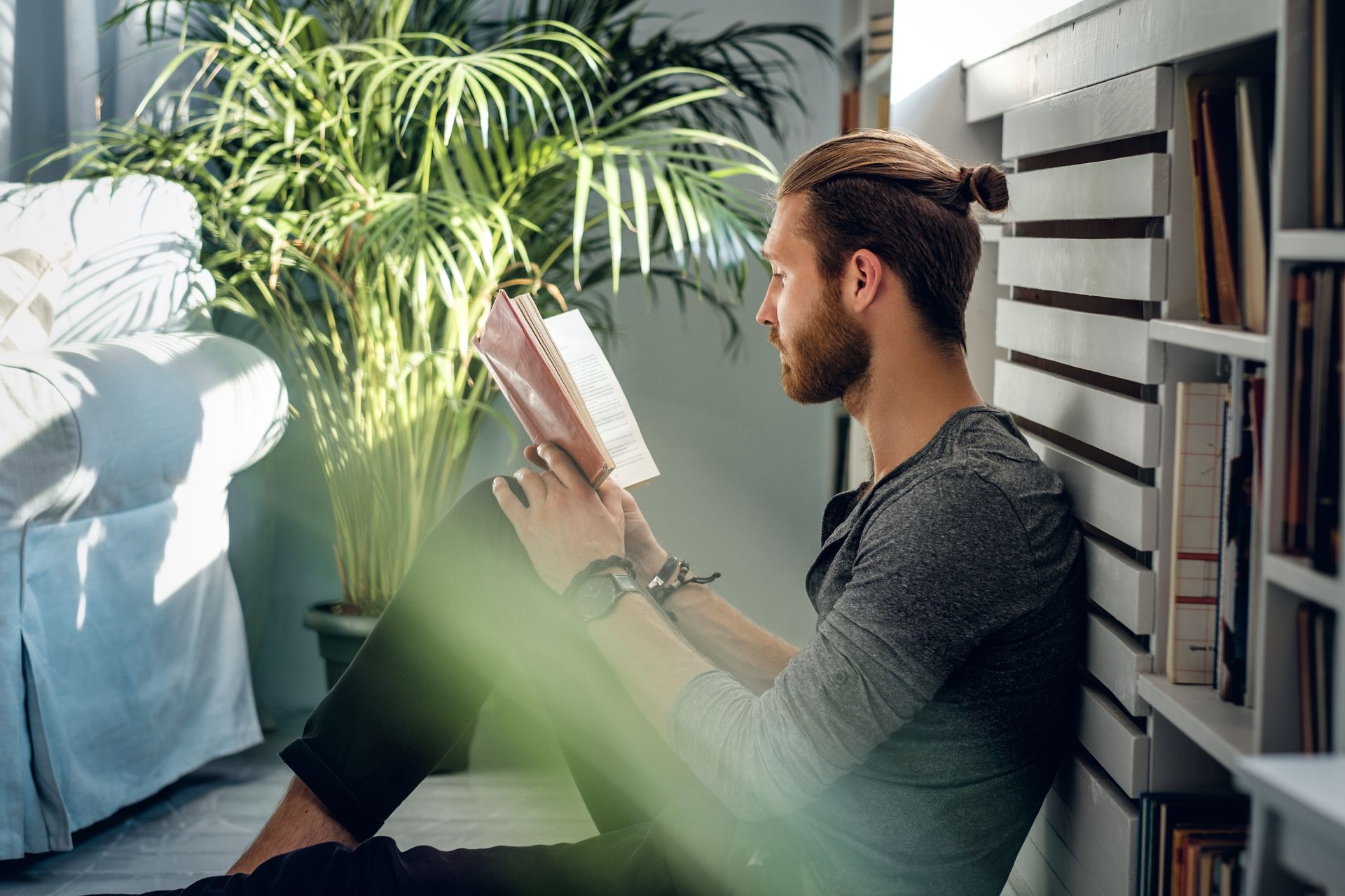 Un homme est assis par terre et lit un livre.