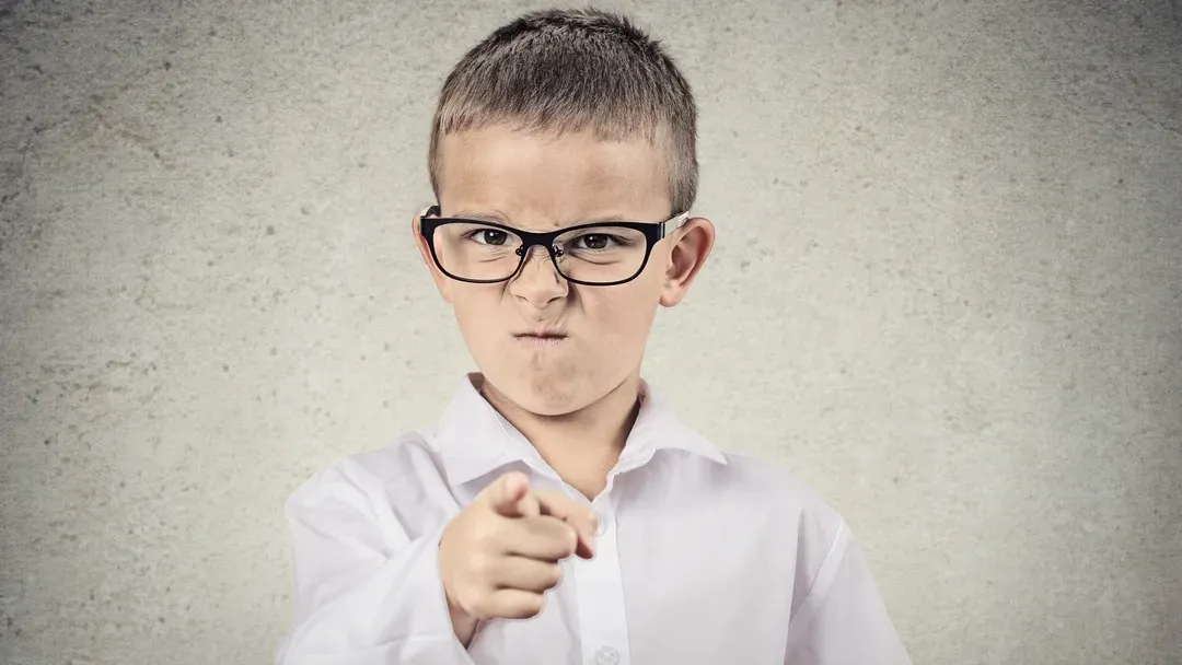 Un jeune garçon portant des lunettes pointe du doigt la caméra.