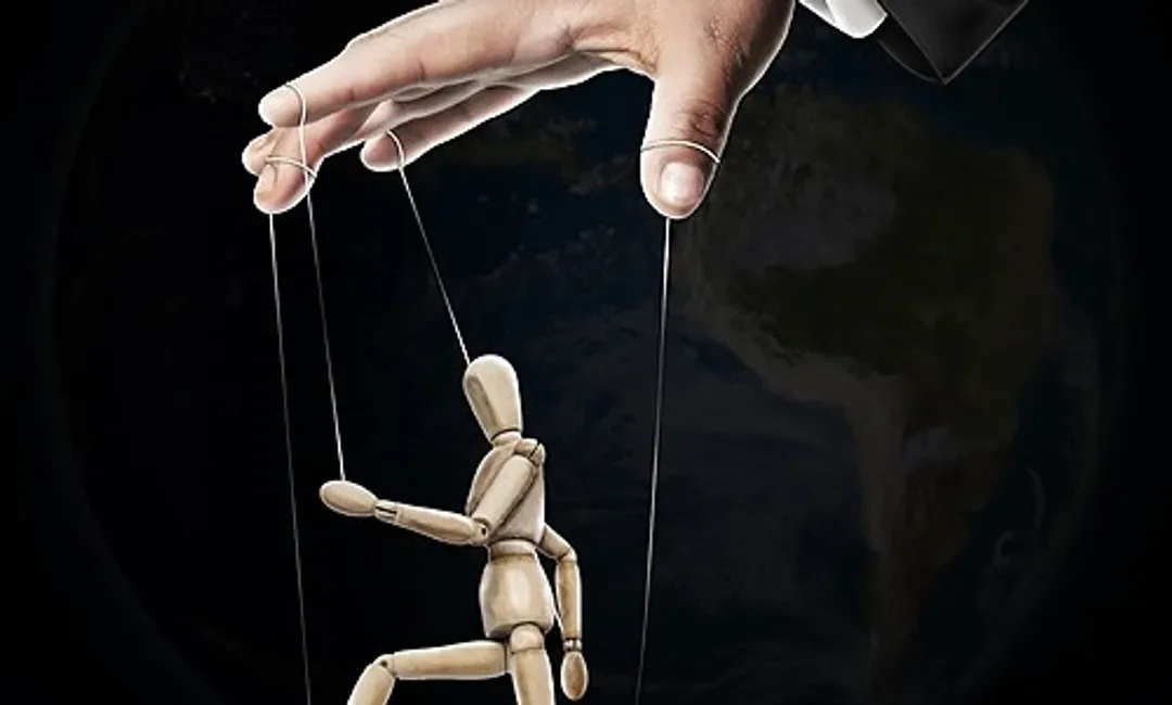 Une main tient une marionnette en bois sur des ficelles.