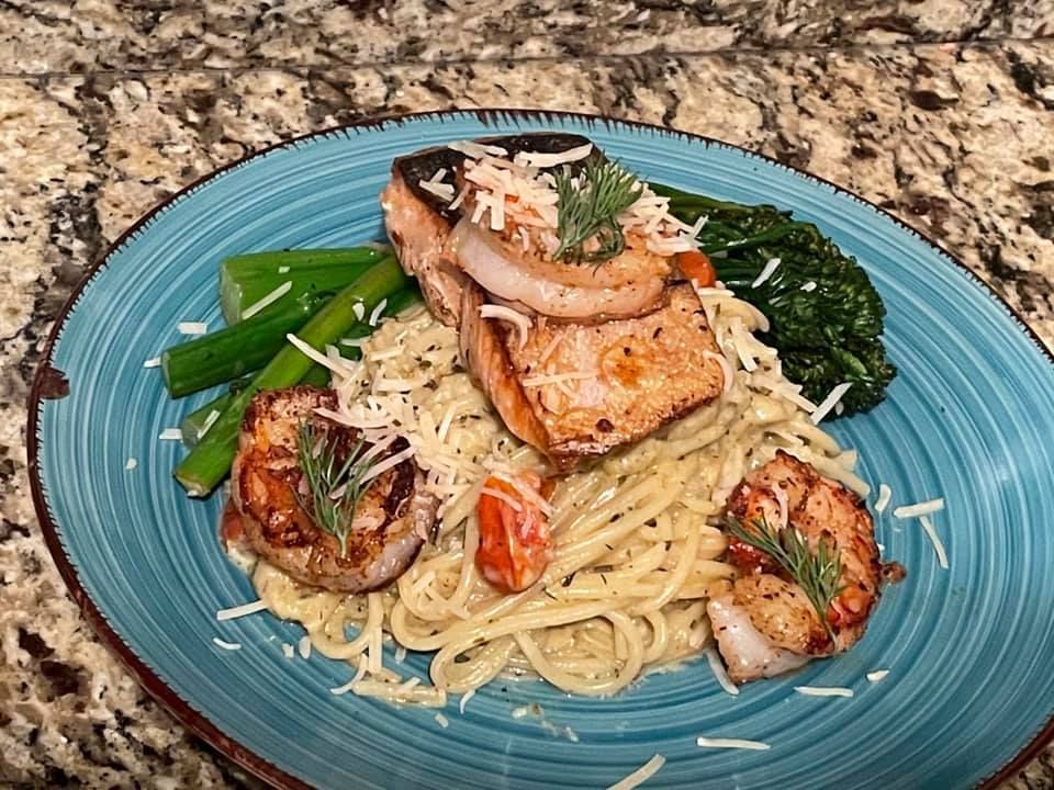 A blue plate topped with noodles , shrimp , and spinach on a counter.