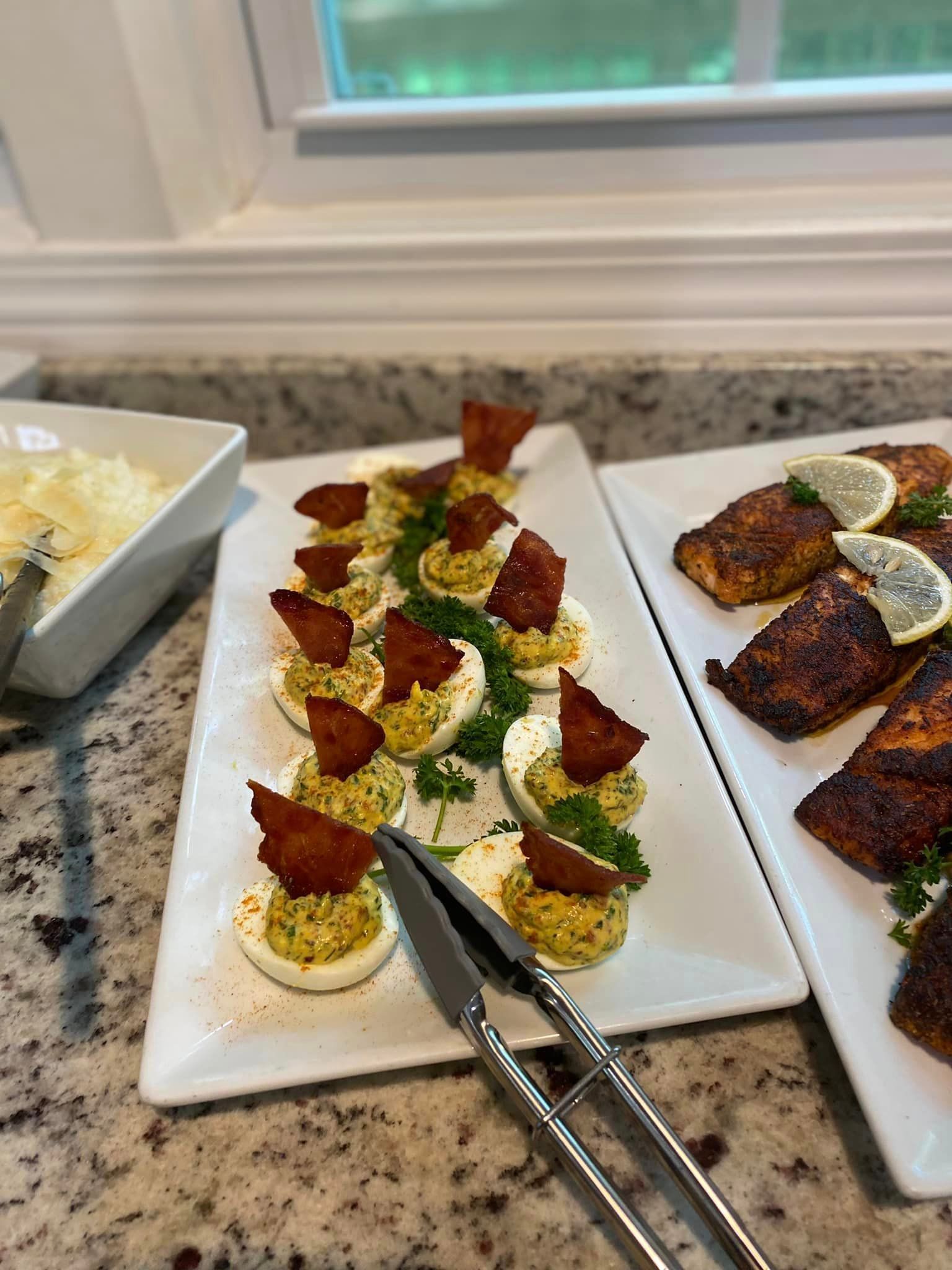 A white plate topped with stuffed eggs and bacon next to a plate of salmon.