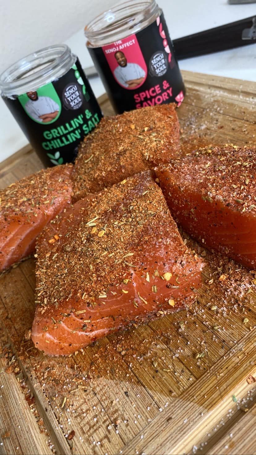 A wooden cutting board topped with salmon and two jars of spices.