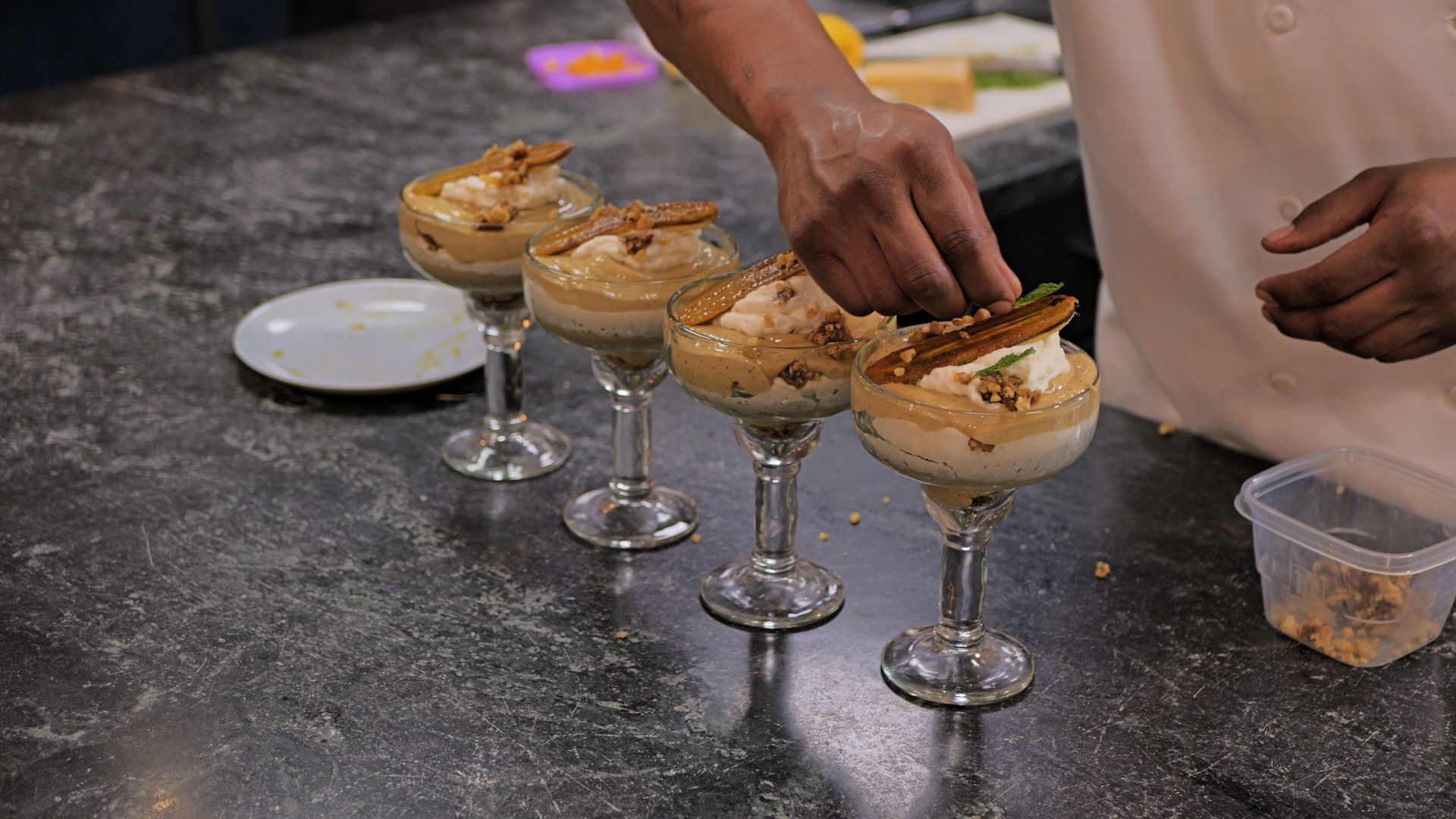 Dessert glasses on a counter while a person tops them with a spoonful of filling