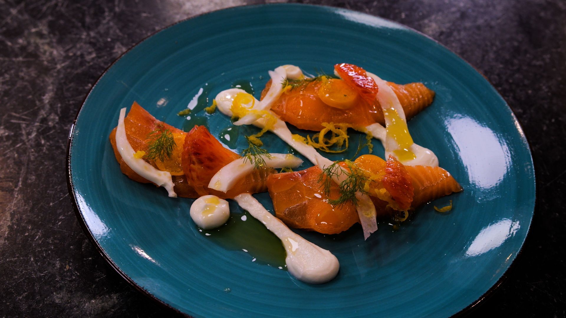 Plated orange-glazed pastry with white cream drizzle on a teal dish