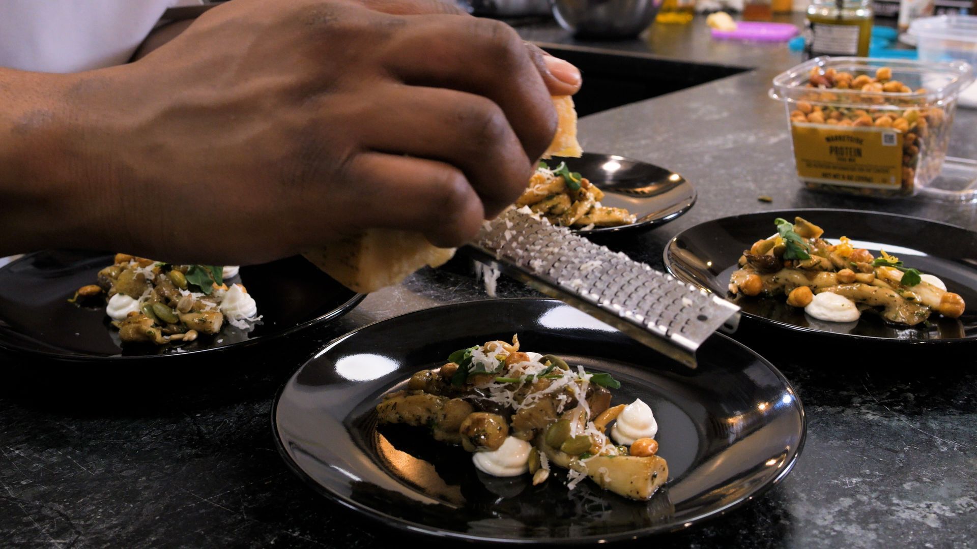 Hand placing garnish on small black plates of food at a restaurant table