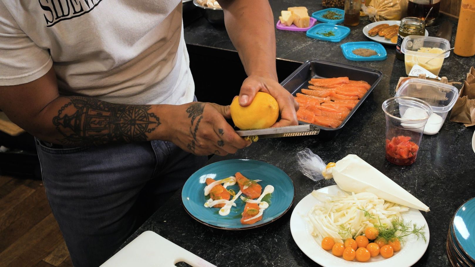 Person arranging fruit on a table with plates of sliced fruit and snacks in a food-prep setting