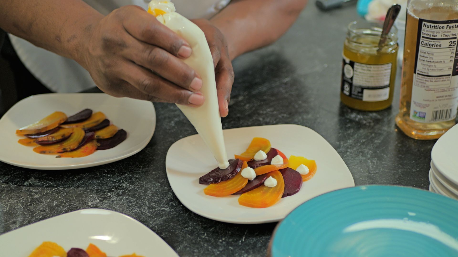Hands piping cream onto colorful plated dessert in a kitchen setting