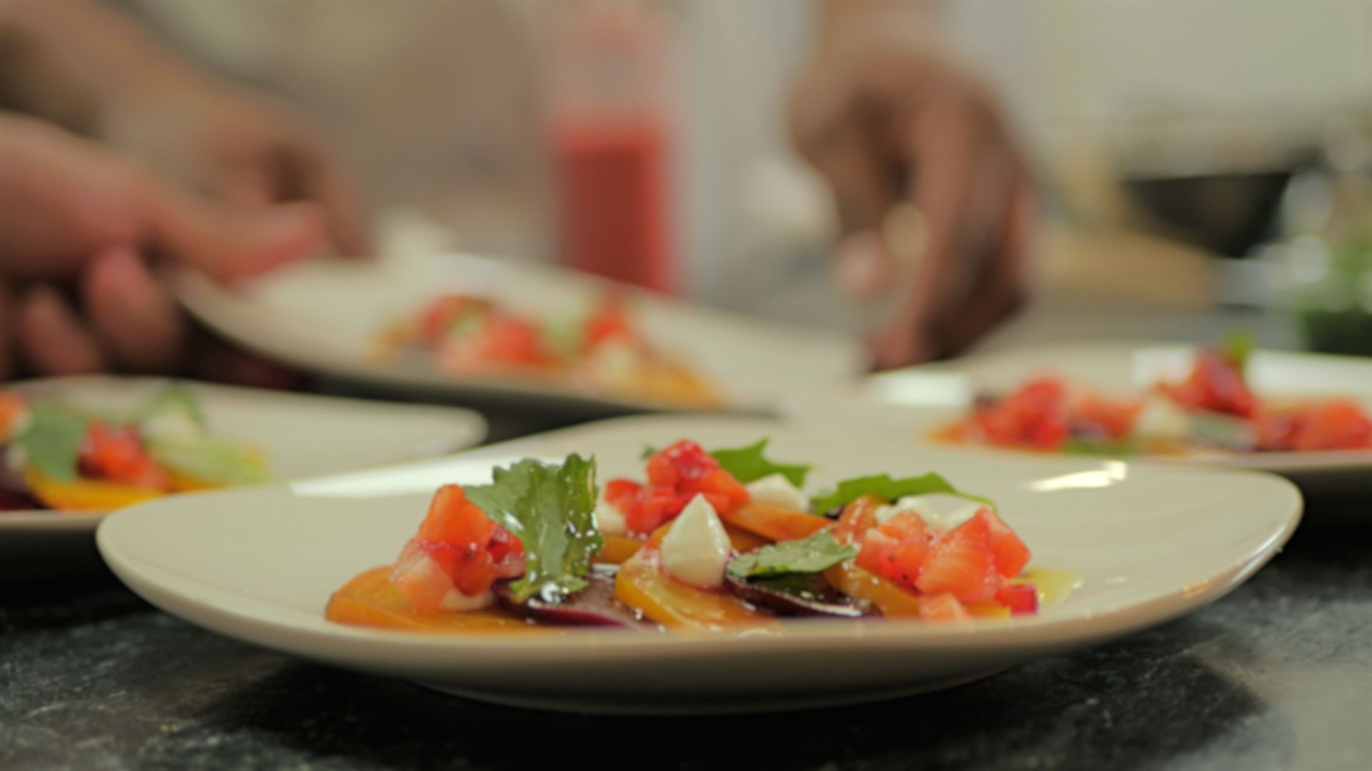 Plated salad with tomatoes and greens being prepared on a kitchen counter
