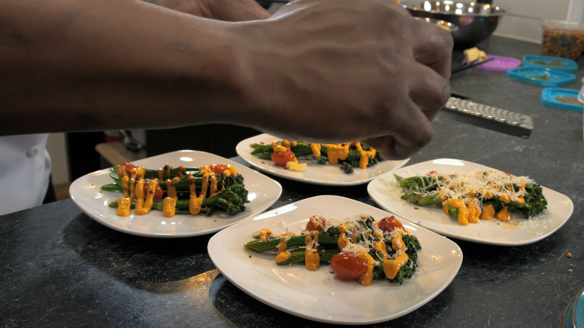 Hands plating colorful appetizers on white plates on a dark countertop