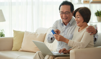 Two smiling older adults lean together over papers at a desk with a laptop nearby.