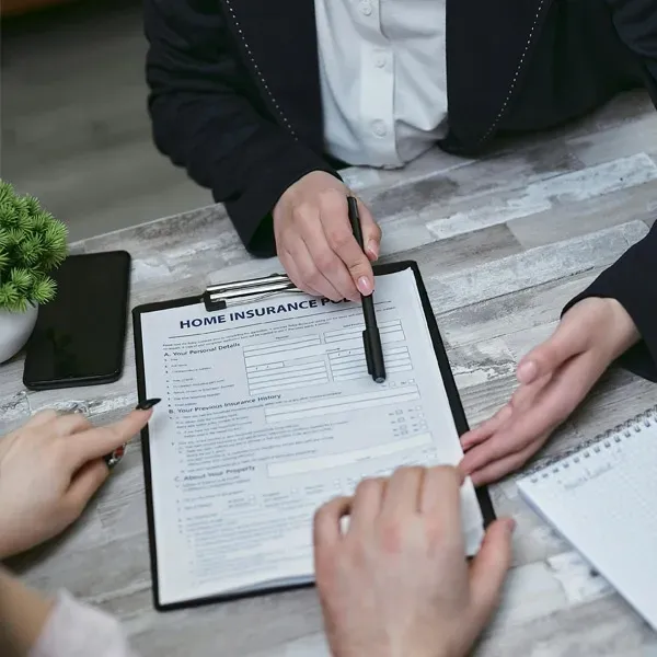 People reviewing a home insurance form at a table with documents and a pen