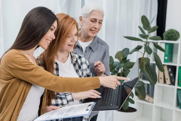 Three people review a laptop and document in a bright office, pointing at the screen.