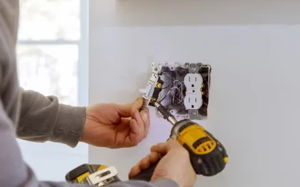 Service of Knights LLC - A man is installing an electrical outlet on a wall with a drill.