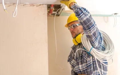 Service of Knights LLC - A man wearing a hard hat and headphones is working on a ceiling.
