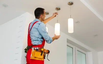 Service of Knights LLC - A man is installing a light fixture on the ceiling of a room.