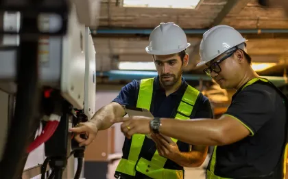 Service of Knights LLC - Two men wearing hard hats and safety vests are working on a machine.