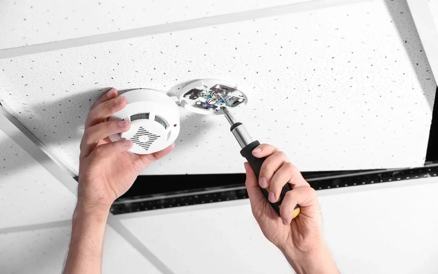 Service of Knights LLC - A person is installing a smoke detector on the ceiling.