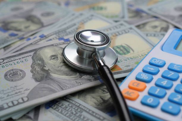 A stethoscope is sitting on top of a pile of money next to a calculator.