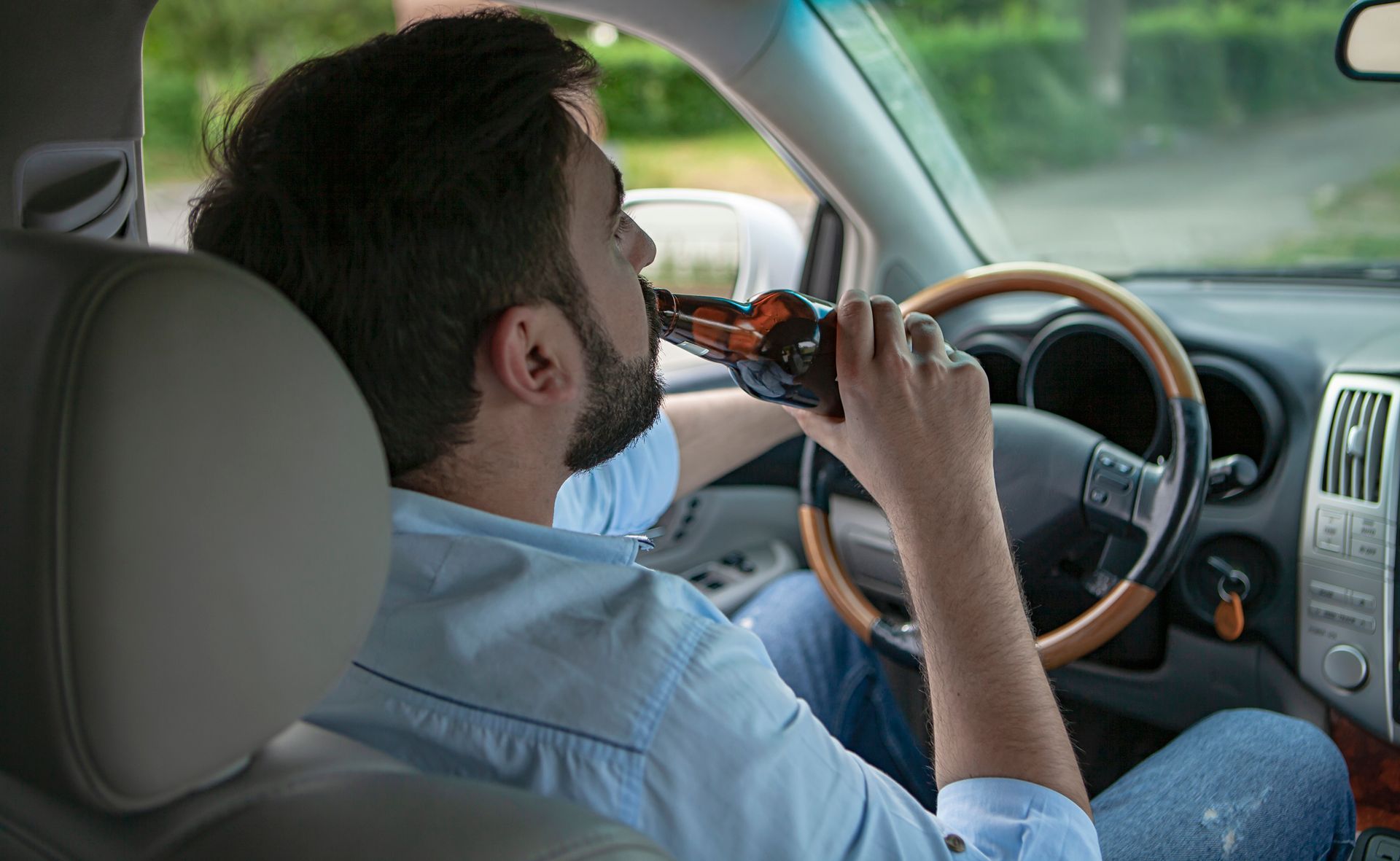 A man is drinking a beer while driving a car.