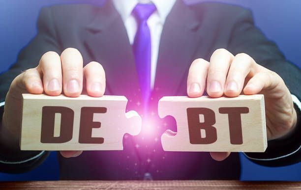 A man in a suit and tie is holding wooden blocks with the words debt and bt written on them.