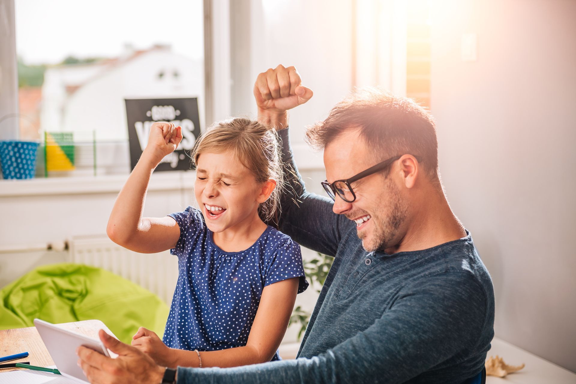A man and a little girl are sitting at a table looking at a tablet.