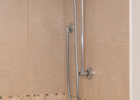 Barra de apoyo cromada para ducha sobre pared de baño alicatada en color beige