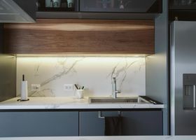 Encimera de cocina moderna con fregadero, iluminación bajo los armarios y un frigorífico a la derecha.