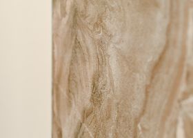 Primer plano de una superficie de piedra o madera con vetas beige y marrón claro y un borde liso color crema a la izquierda.