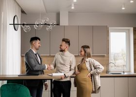Tres personas conversan en una cocina moderna; una de ellas está visiblemente embarazada.