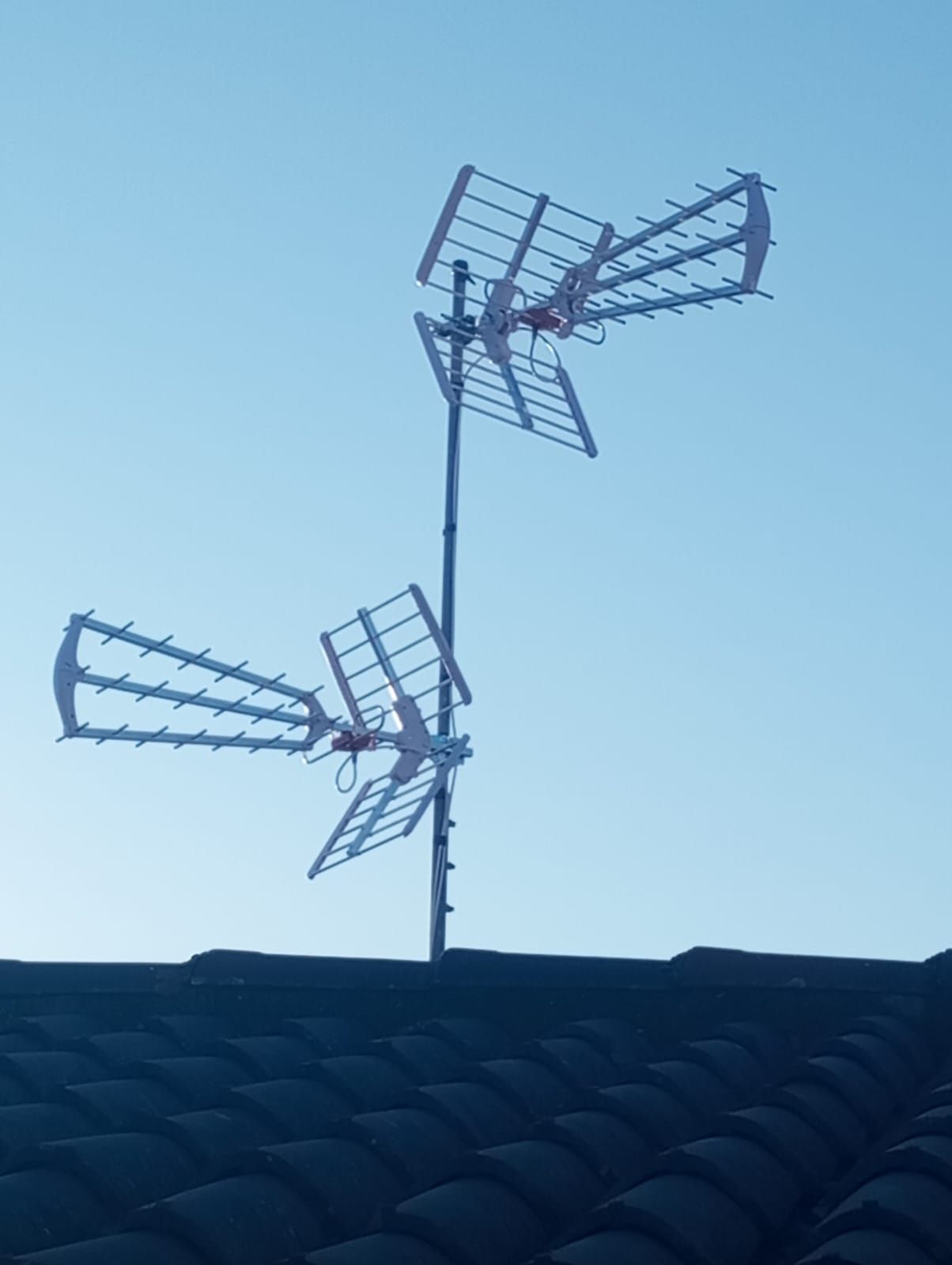 Due antenne TV multidirezionali su un tetto contro un cielo azzurro e terso.