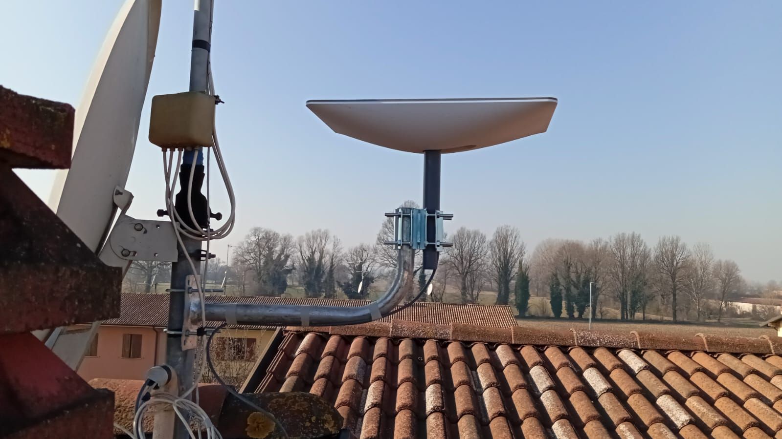 Antenne paraboliche sul tetto con alberi e cielo sullo sfondo.