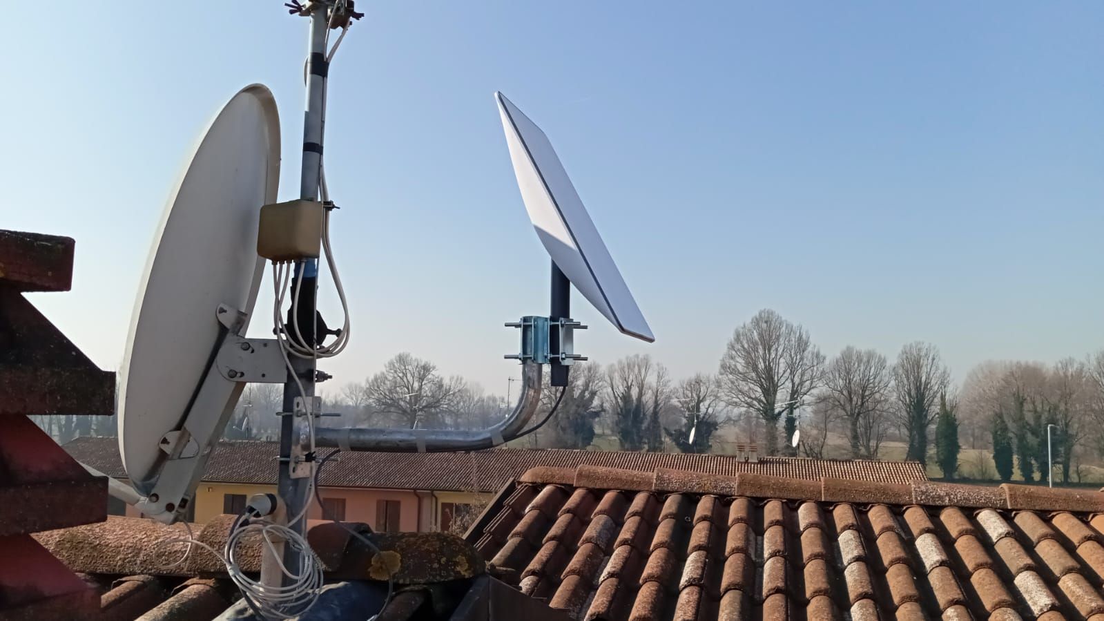 Due parabole satellitari su un tetto, una rotonda e una rettangolare, contro un cielo azzurro.