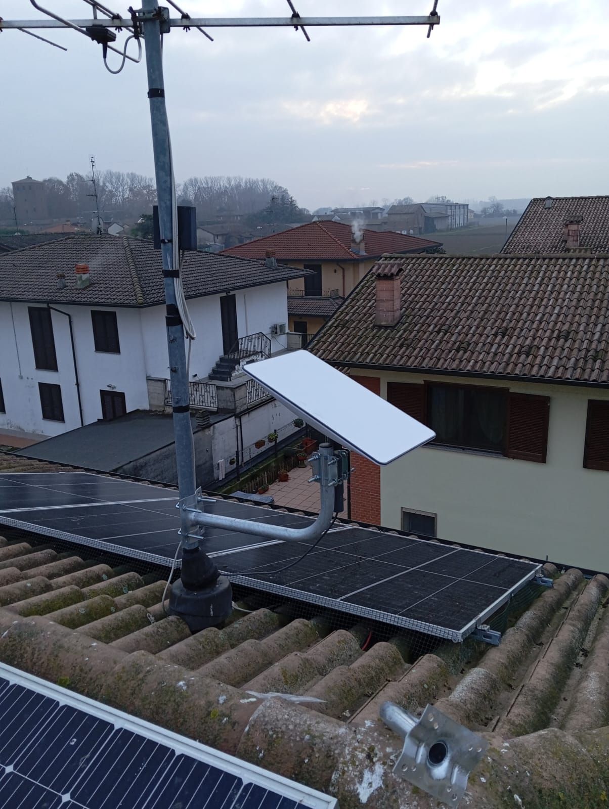 Antenna parabolica bianca montata sopra i pannelli solari su un tetto. Edifici e cielo sullo sfondo.