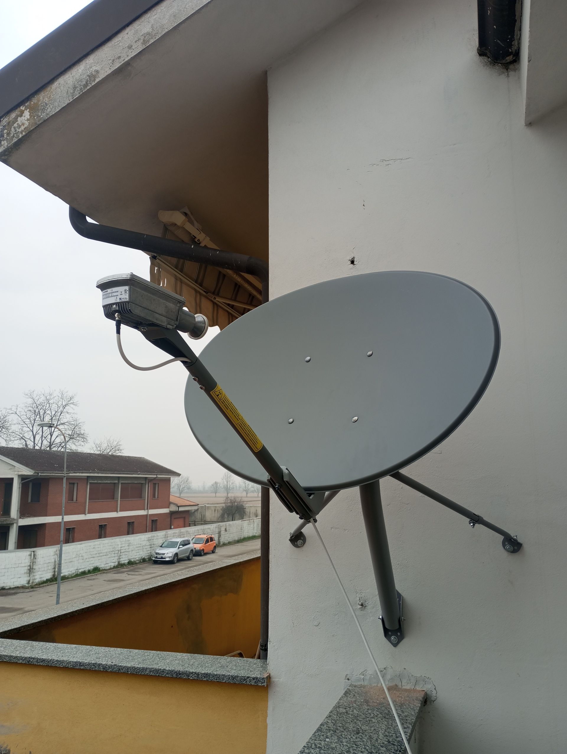Parabola satellitare montata sulla parete esterna di un edificio, puntata verso il cielo, in una giornata nuvolosa.