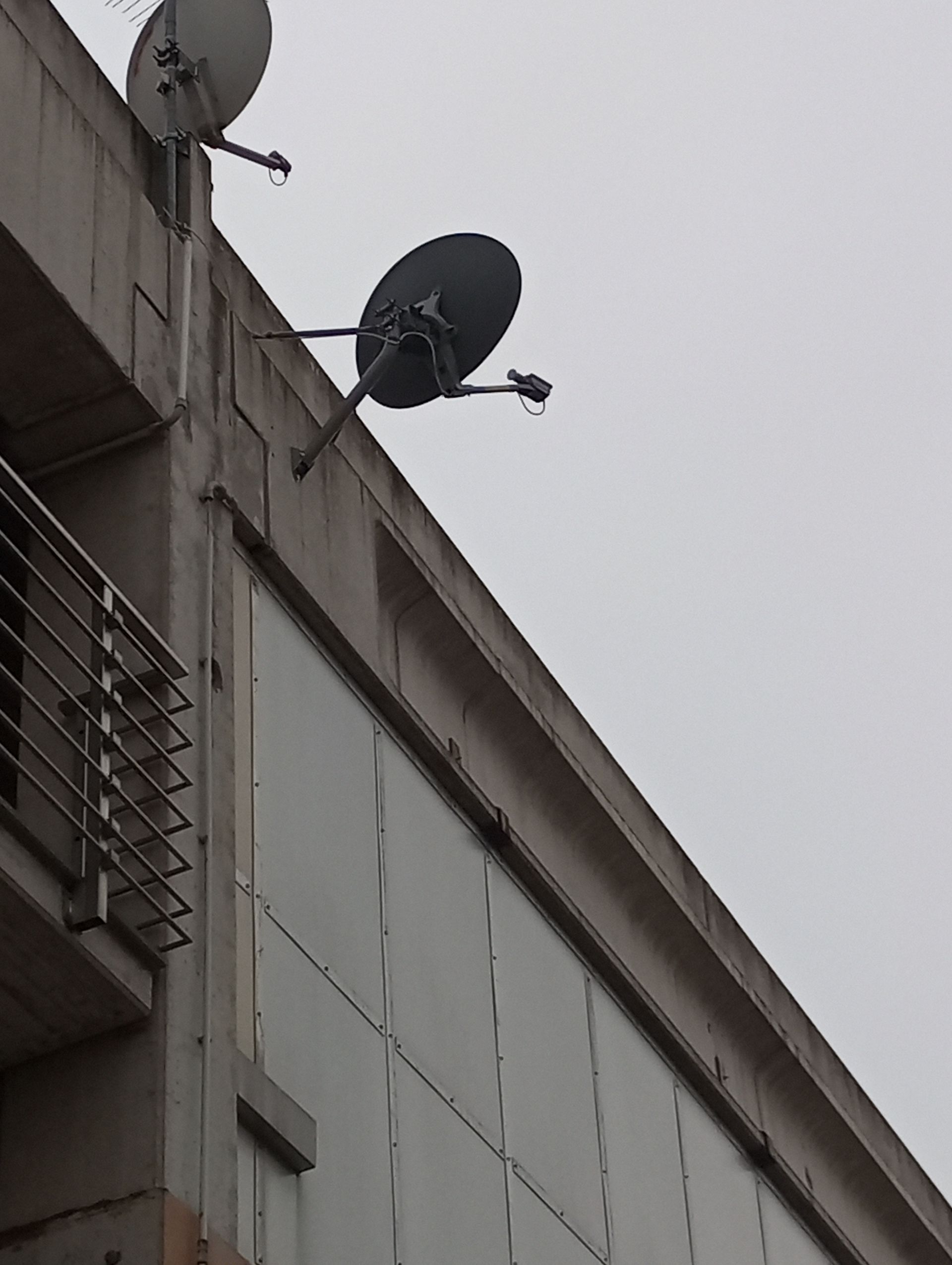 Due parabole satellitari montate sull'angolo di un edificio in cemento contro un cielo nuvoloso.