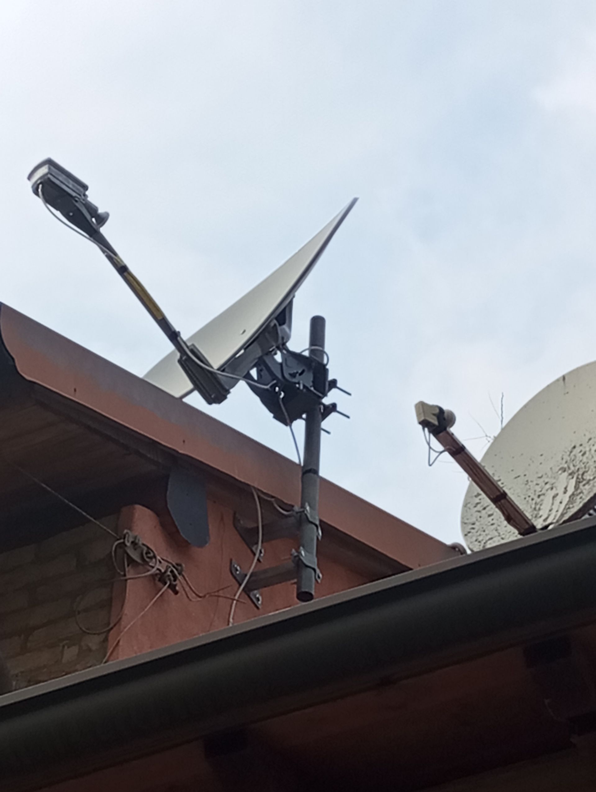 Due parabole satellitari montate su un tetto marrone, angolate verso il cielo. Parabola grigia e accessori di montaggio neri.