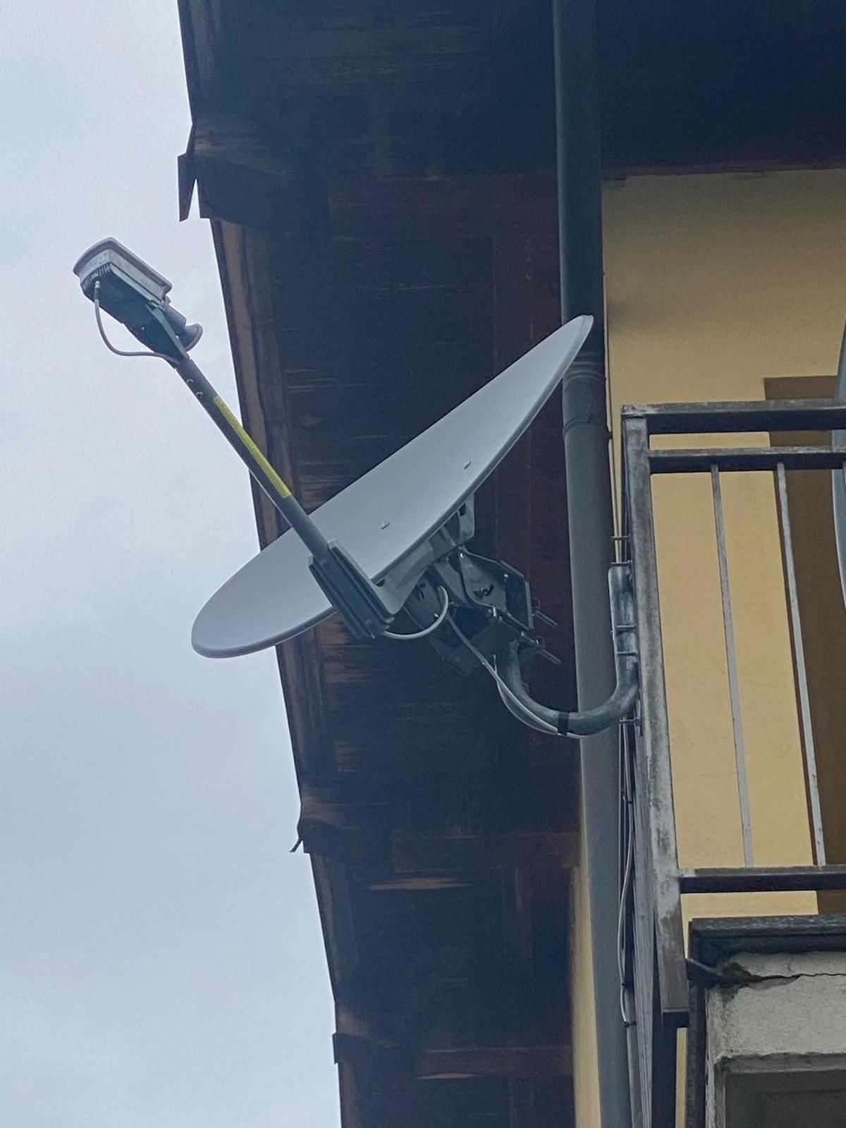 Parabola satellitare montata sulla parte esterna di un edificio, vicino a una grondaia e a un balcone.