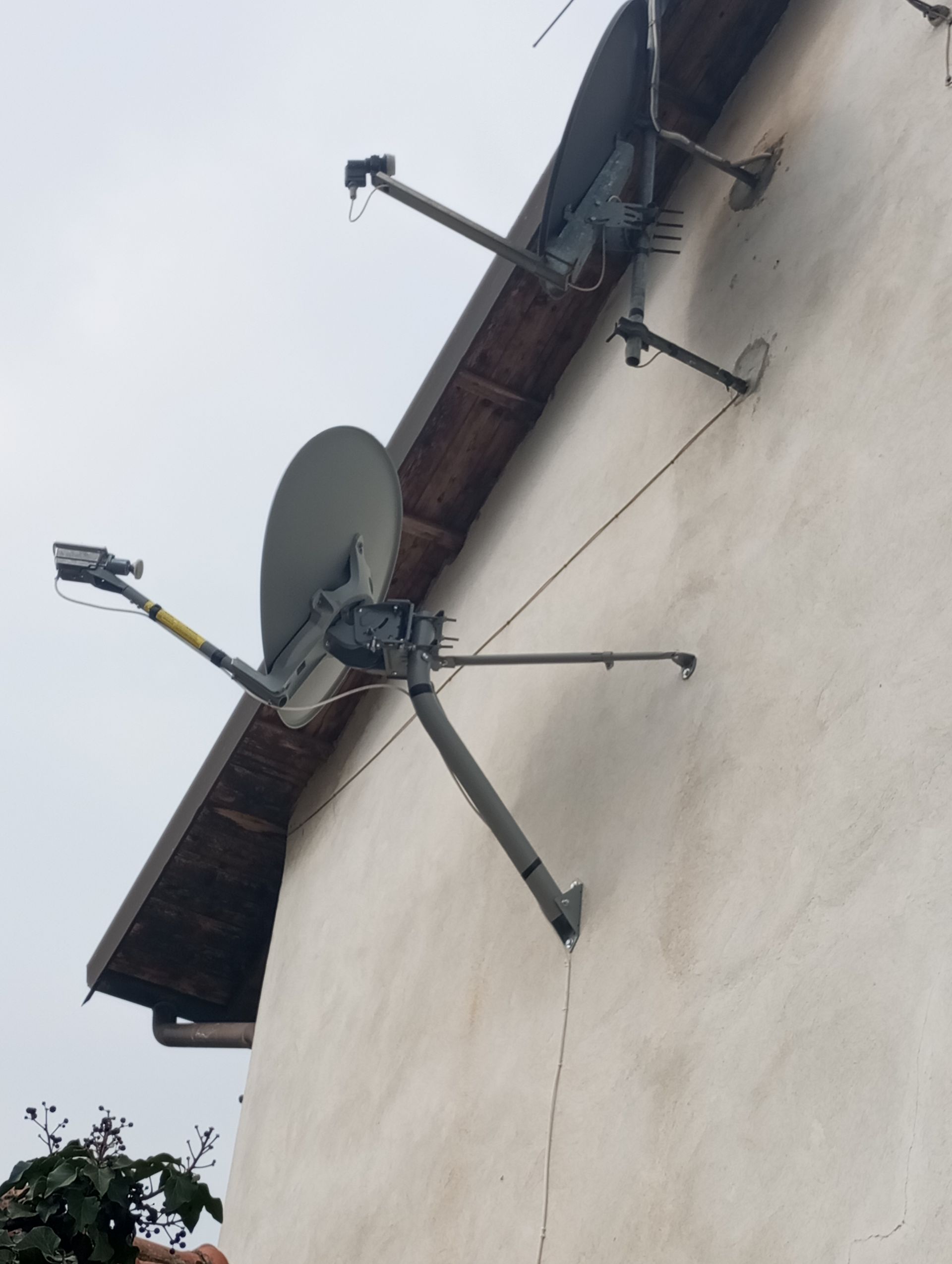 Parabole satellitari montate sulla facciata esterna di un edificio bianco, sotto un tetto. Dalle parabole partono i cavi.