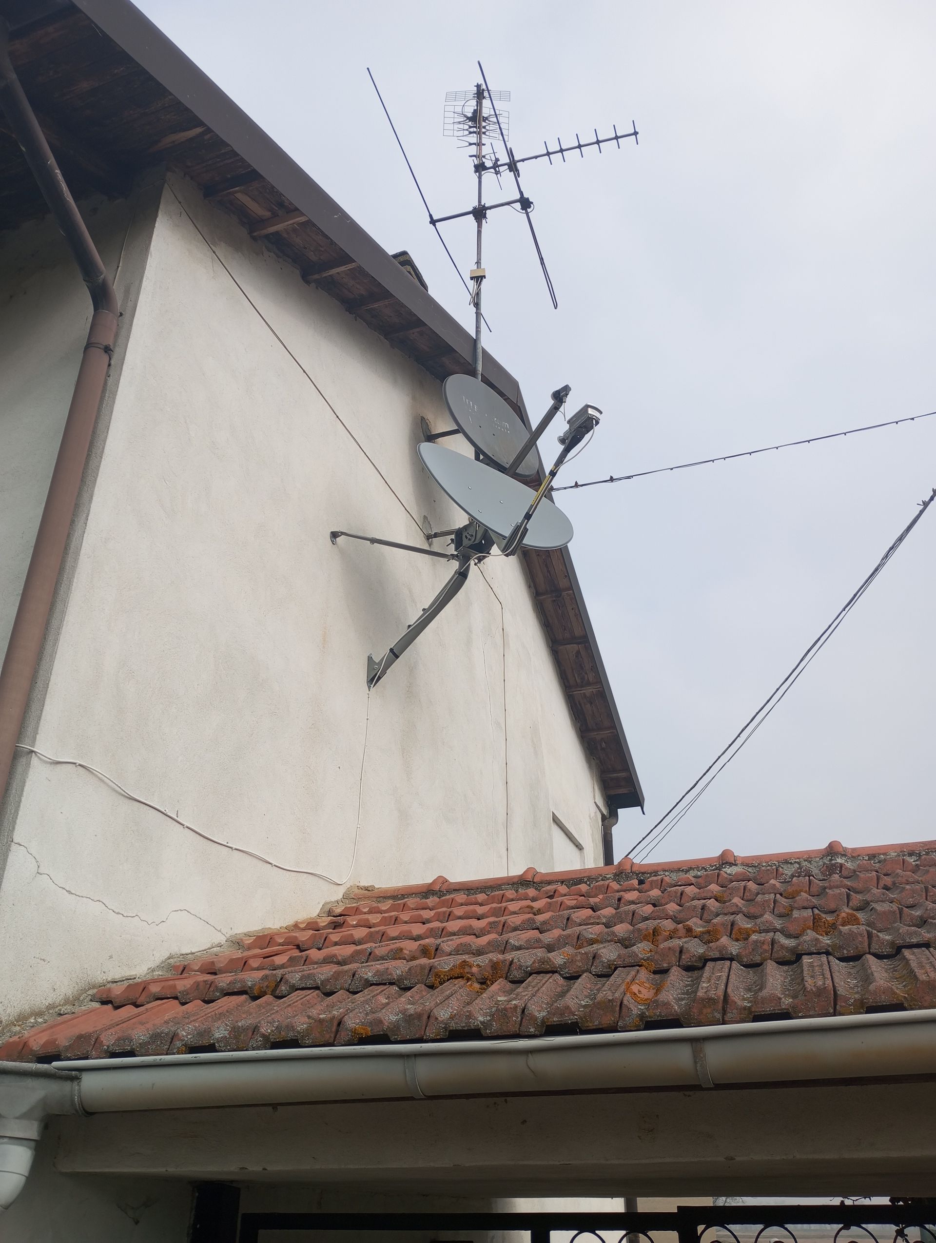 Antenne televisive all'esterno di un edificio. Due parabole satellitari, un'antenna e cavi elettrici fissati a una parete beige.