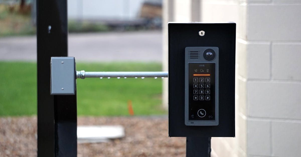 Cancello di sicurezza nero con tastiera e citofono, montato su un palo. La tastiera grigia visualizza numeri e testo rosso.