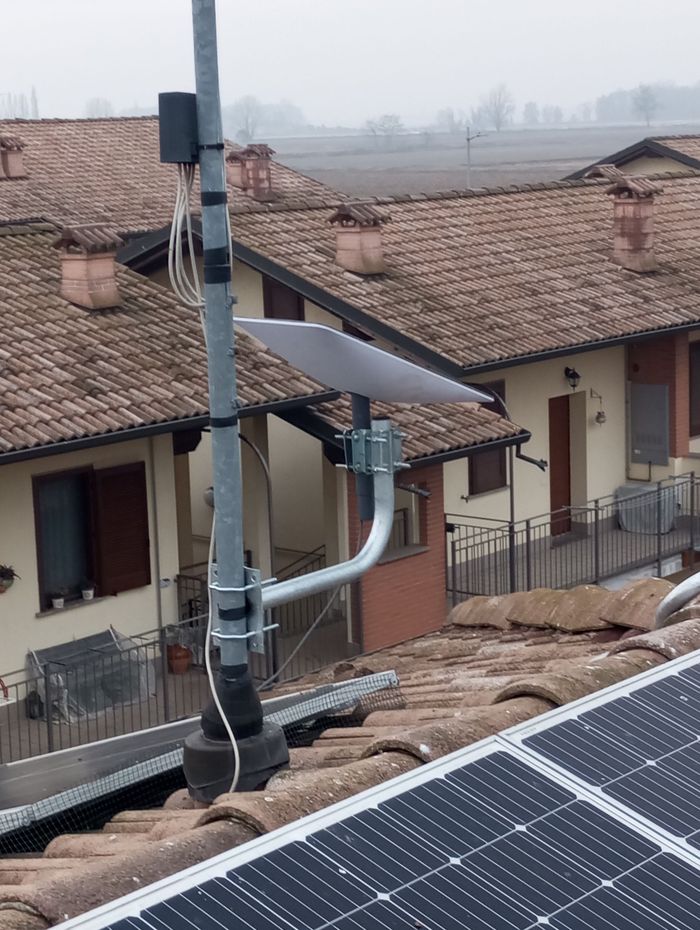 Antenna montata su un tetto con pannelli solari, rivolta verso un paesaggio rurale.