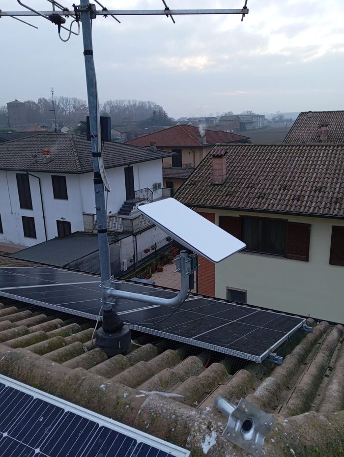 Antenna e parabola satellitare su un tetto con pannelli solari, di fronte alle case in condizioni di cielo coperto.