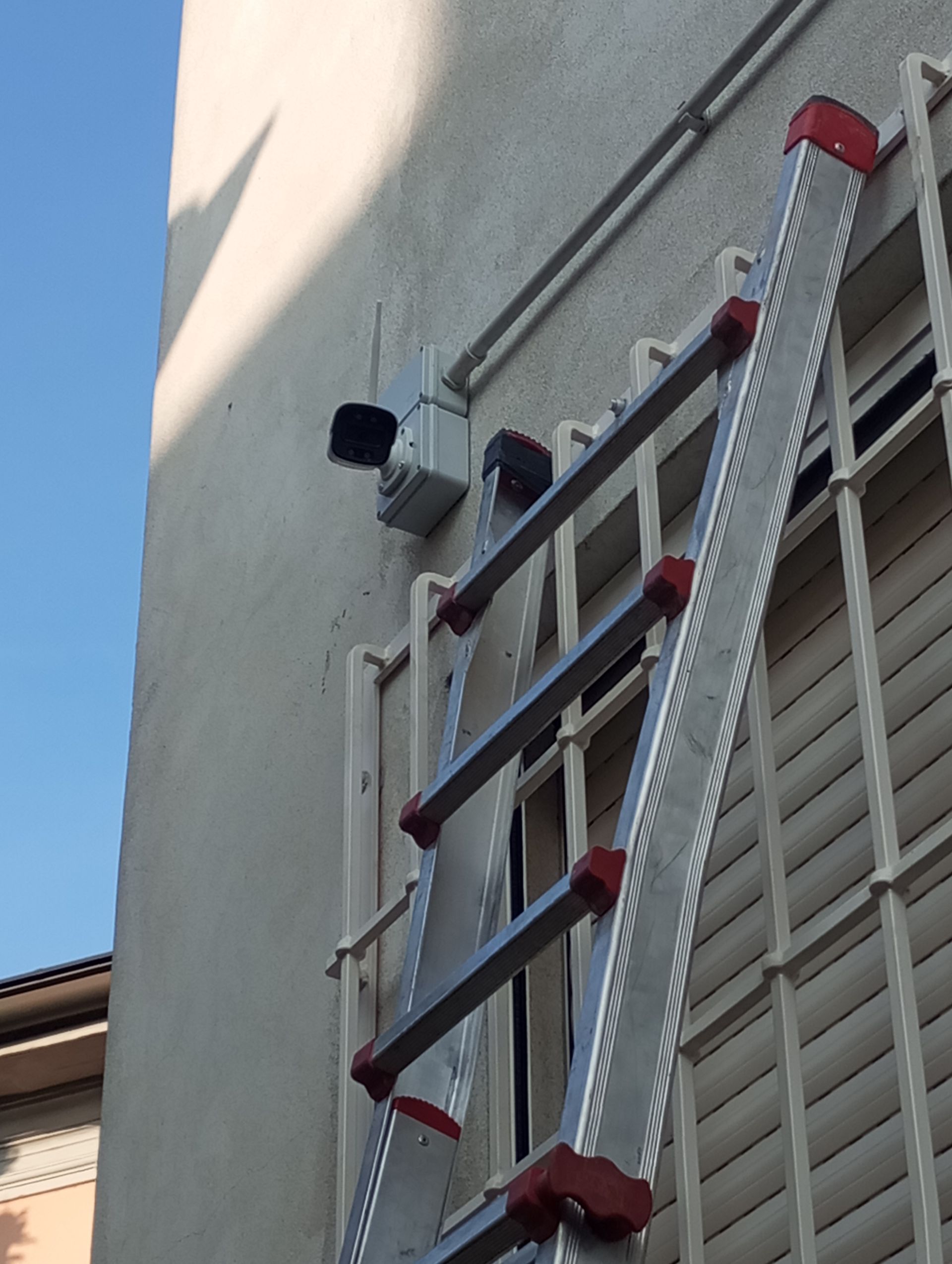Scala appoggiata al muro di un edificio con una telecamera di sicurezza montata.