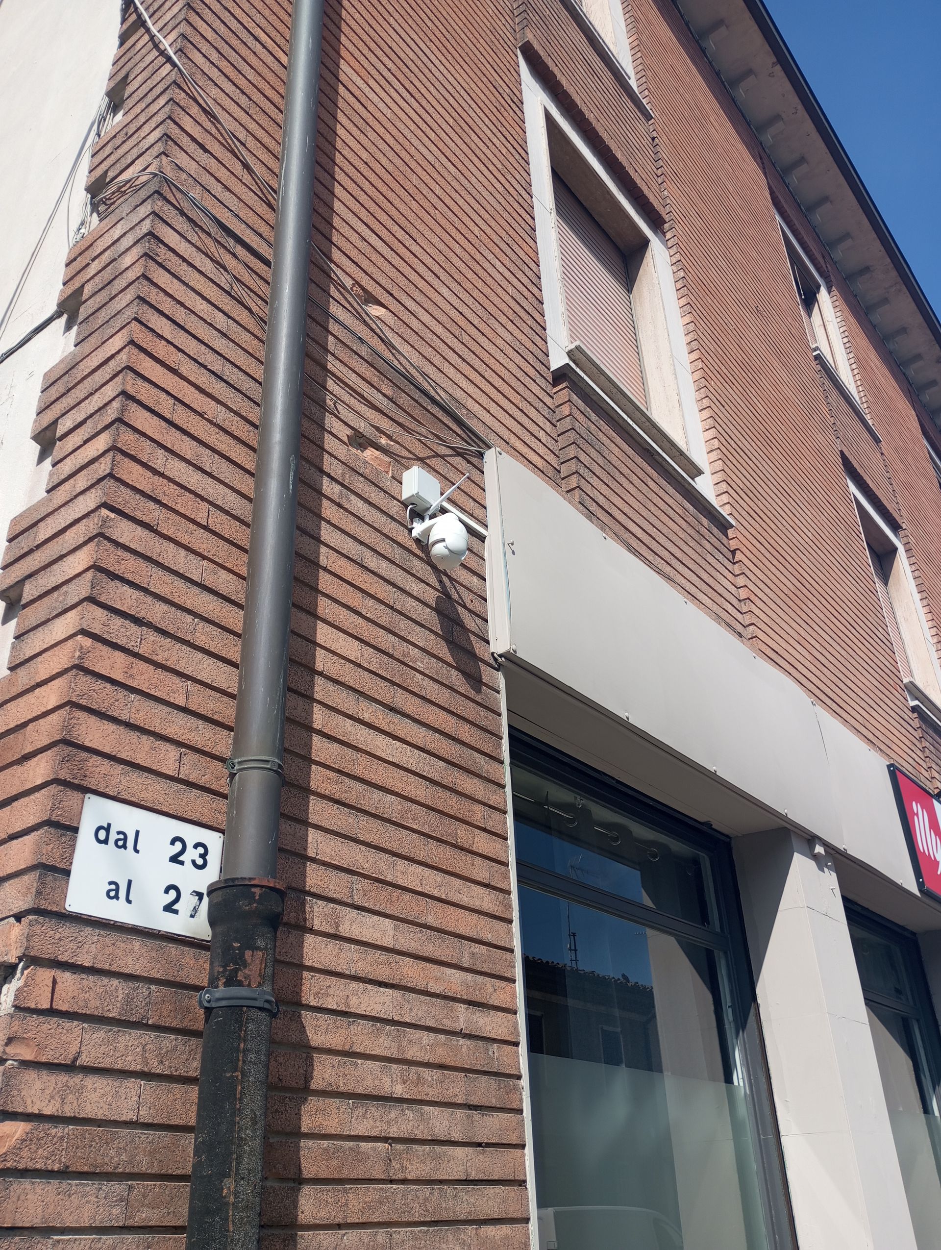 Angolo di un edificio in mattoni con una telecamera di sorveglianza, una grondaia e un cartello.