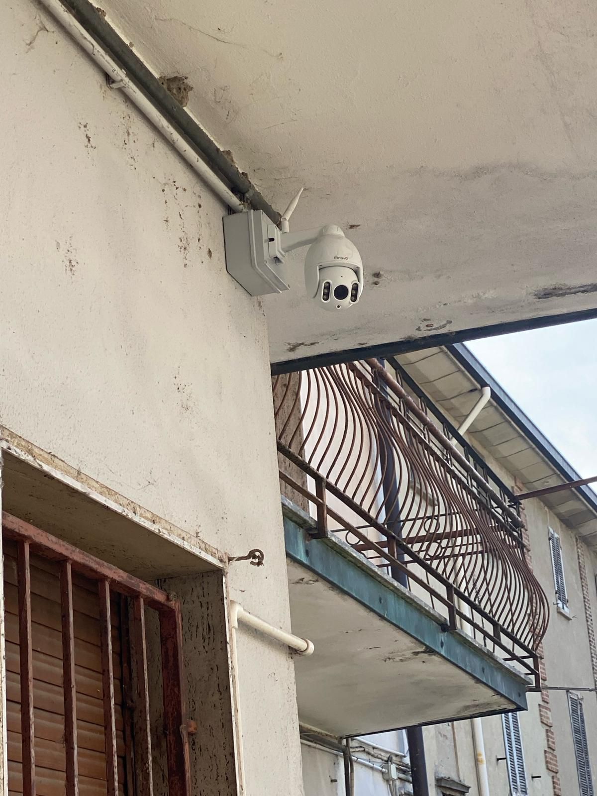 Telecamera di sicurezza montata sulla parete esterna di un edificio, con un balcone sullo sfondo.