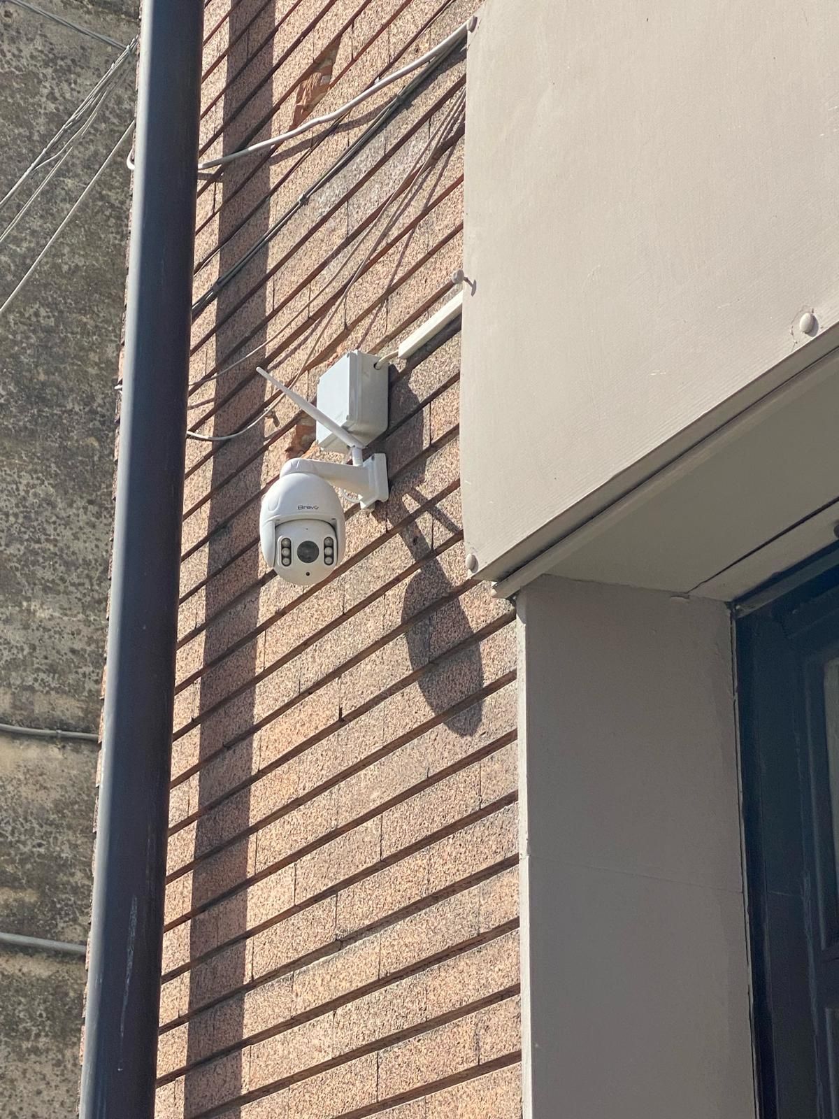 Telecamera di sicurezza montata su un muro di mattoni, accanto all'ingresso di un edificio.
