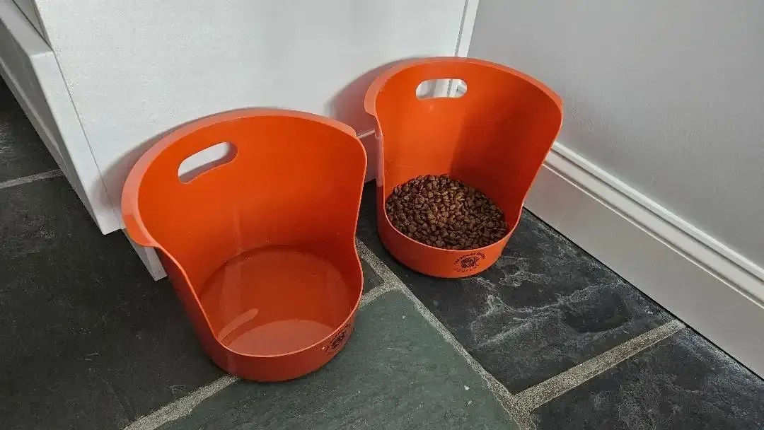 Orange Booga Bucket feeders, one empty and one filled with dry dog food.