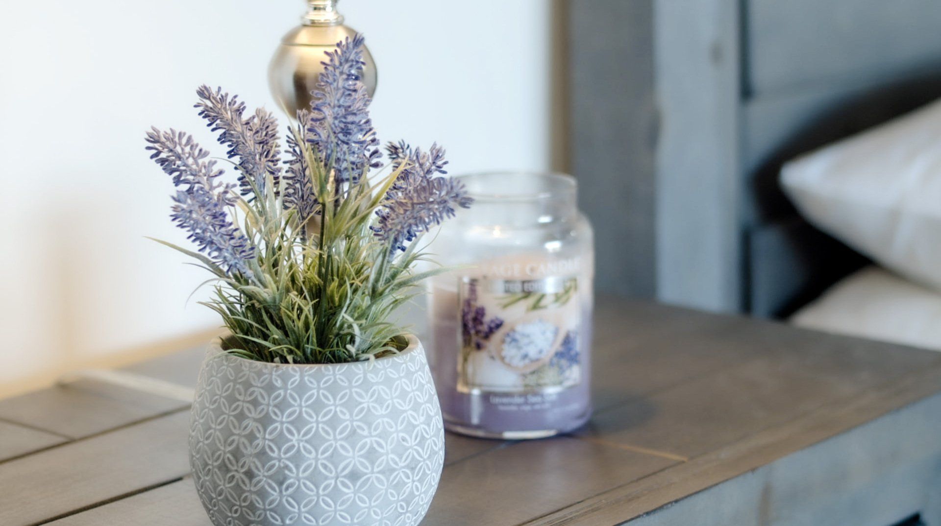 Ramo de lavanda en un jarrón blanco texturizado sobre una mesa de madera junto a un portavelas.