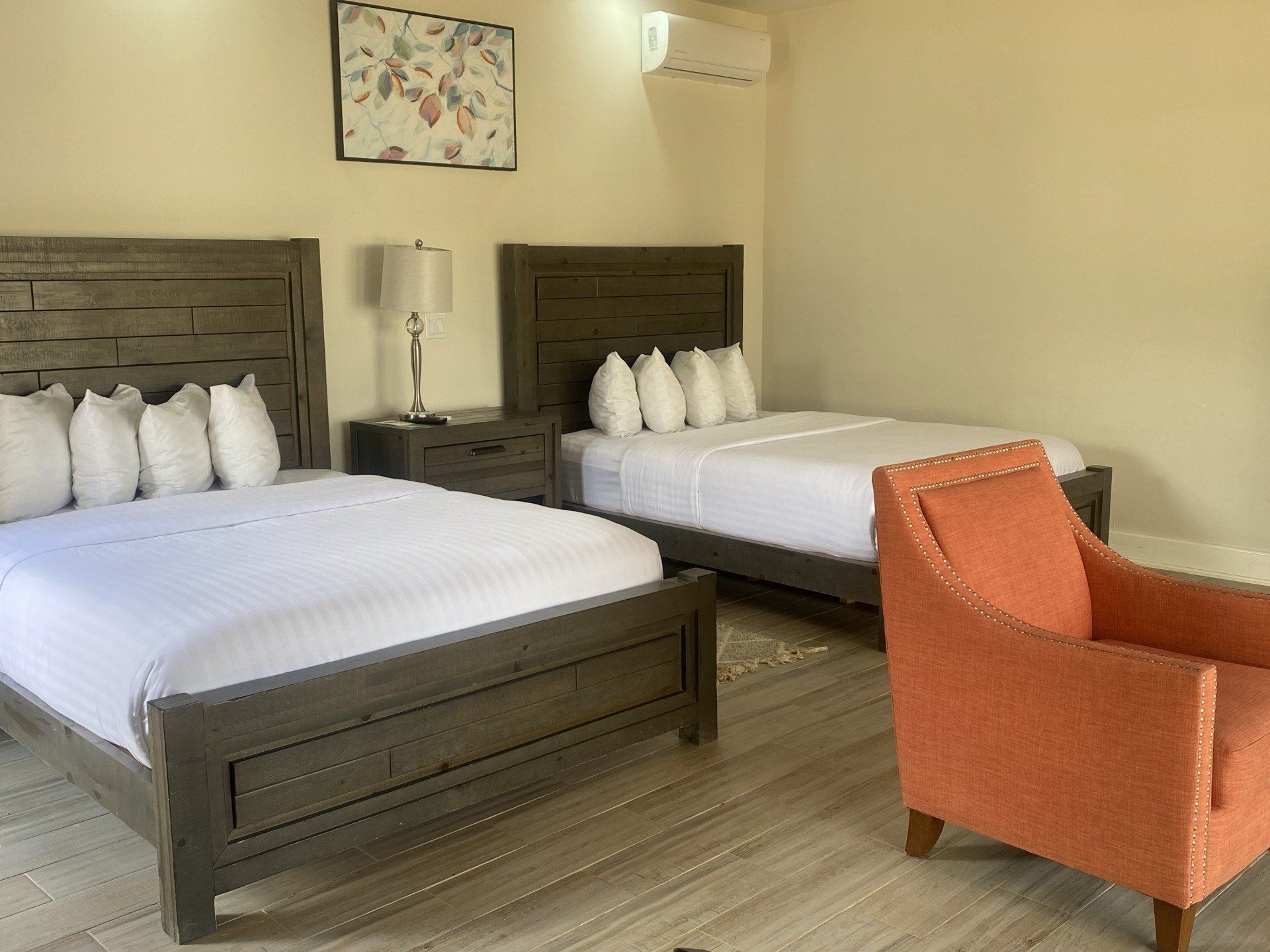 Habitación de hotel con dos camas, ropa de cama blanca y un sillón naranja junto a una mesita.